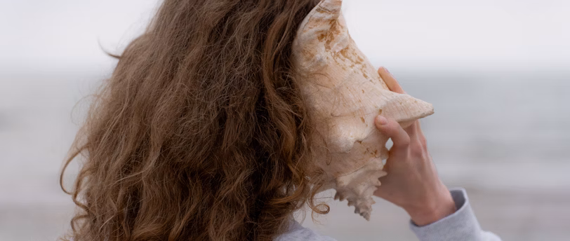 An image of a young girl holding a seashell to her ear, listening for the sound it makes