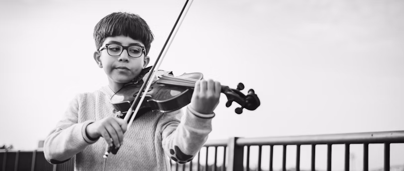 An image of a young boy practising the violin with a bemused expression